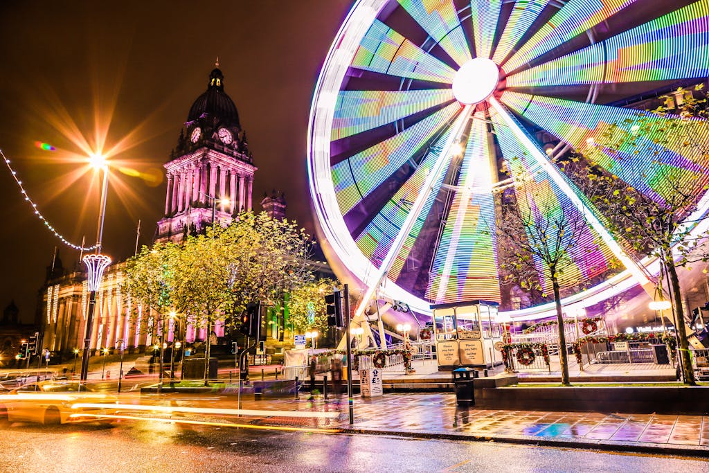 Vibrant night scene featuring Leeds Town Hall and illuminated Ferris Wheel, showcasing colorful city life.